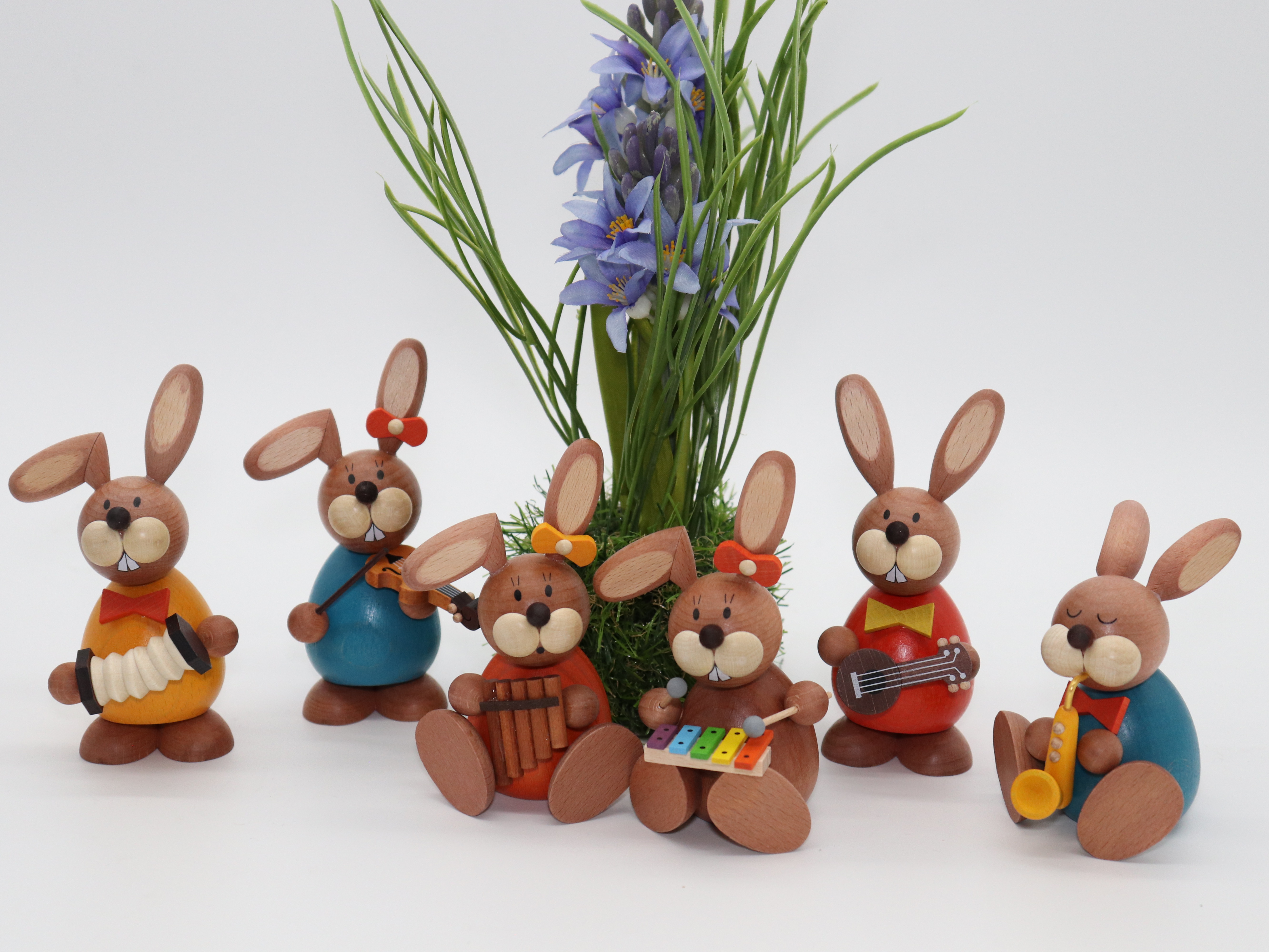 Deko Osterhasen aus Holz, sitzend vor einem Strauß Blumen und jeweils einem anderen Musikinstrument in dewr Hand.