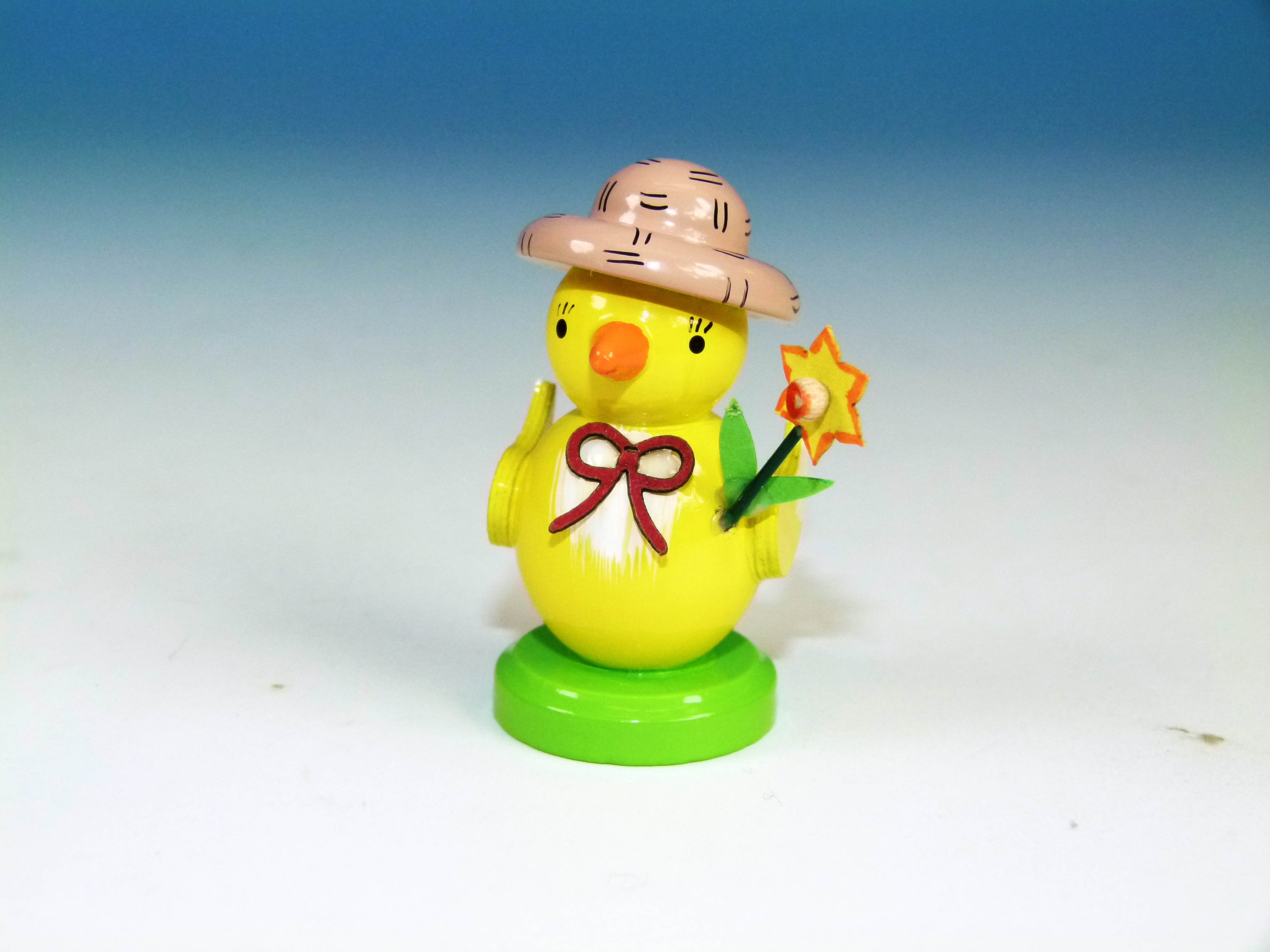 Küken mit Stroh-Hut, roter Schleife und Osterglocke auf einem Sockel als Osterschmuck