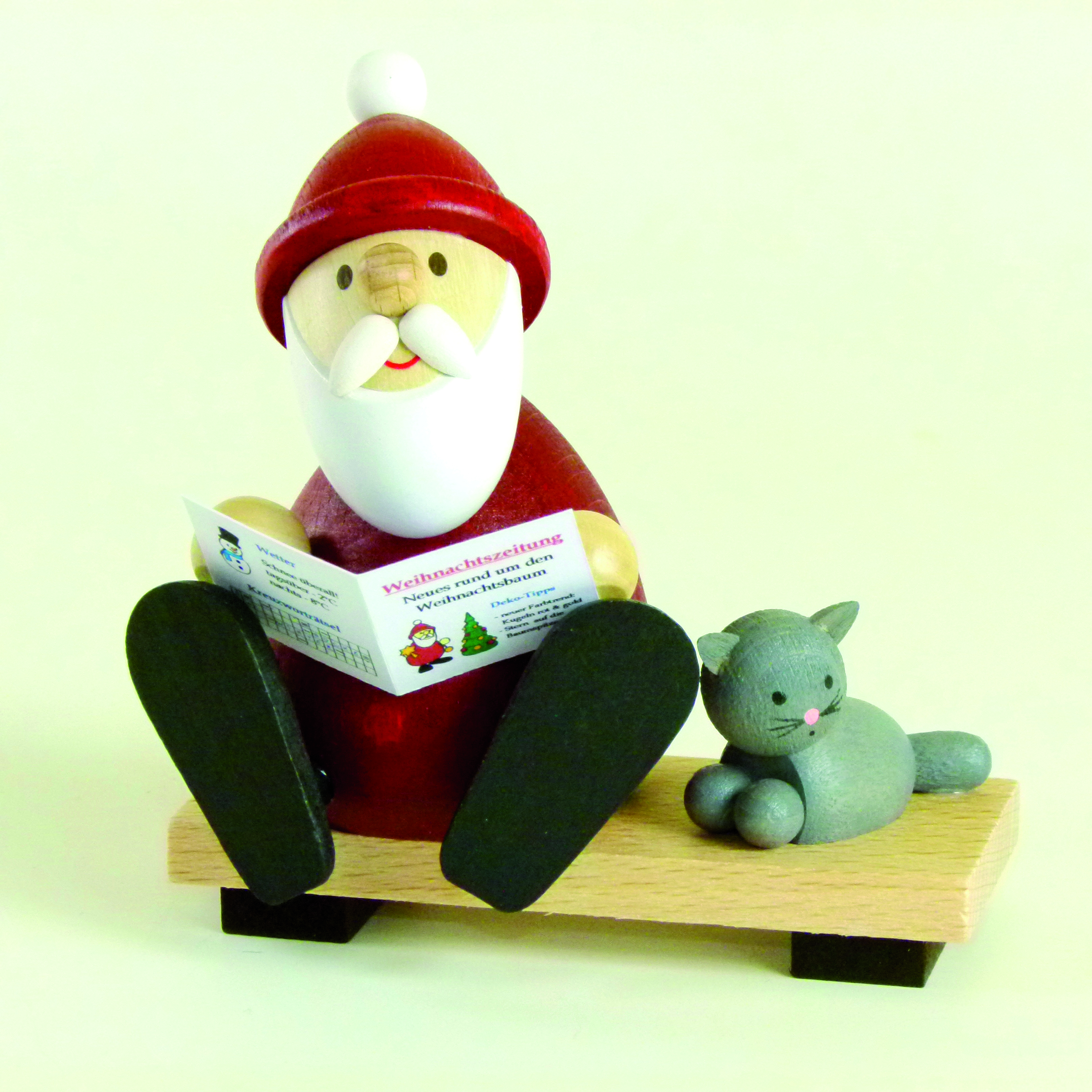Weihnachtsmann modern auf Bank mit Zeitung und Katze als Tischdeko